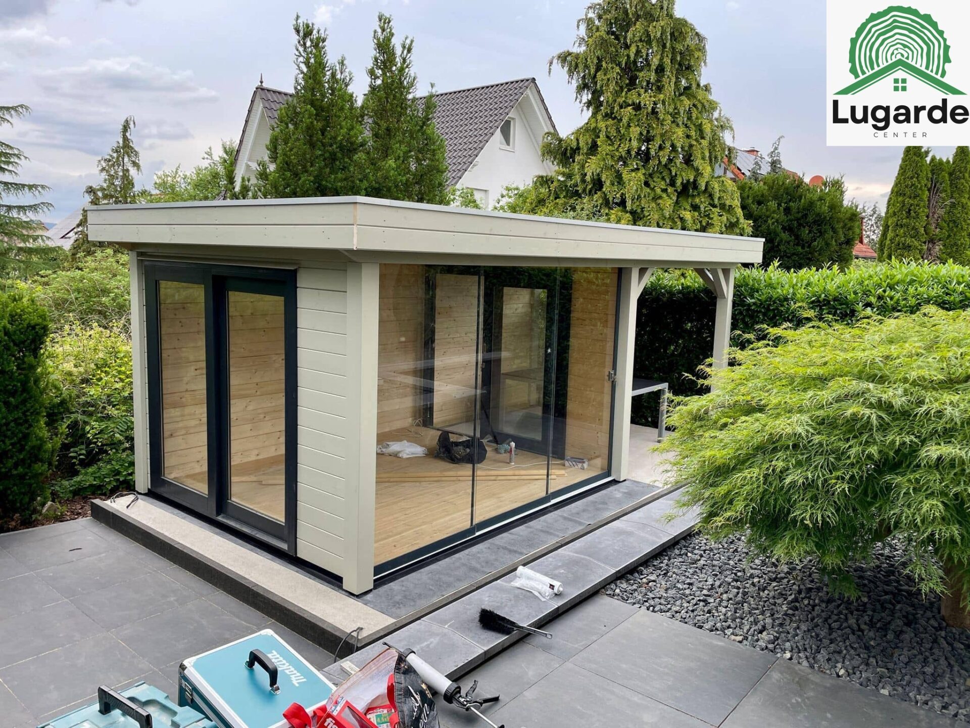 Lugarde Pro System Flachdachhaus in Kieselgrau, große Glasfront, Dachüberstand mit Sitzecke, Outdoor-Grillbereich – Frontansicht.