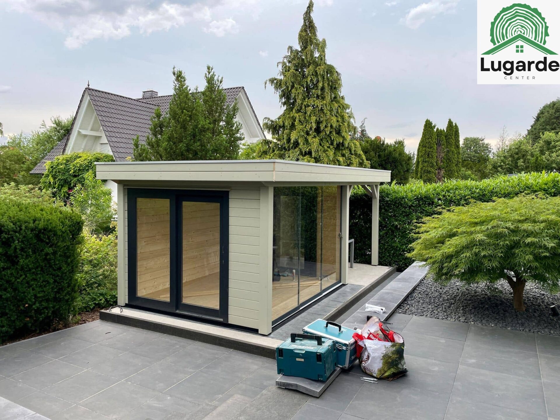 Gartenintegration: Flachdachhaus Kieselgrau, Glasfront zur Terrasse; Dachüberstand schützt Sitzecke, Outdoor-Grillen daneben.