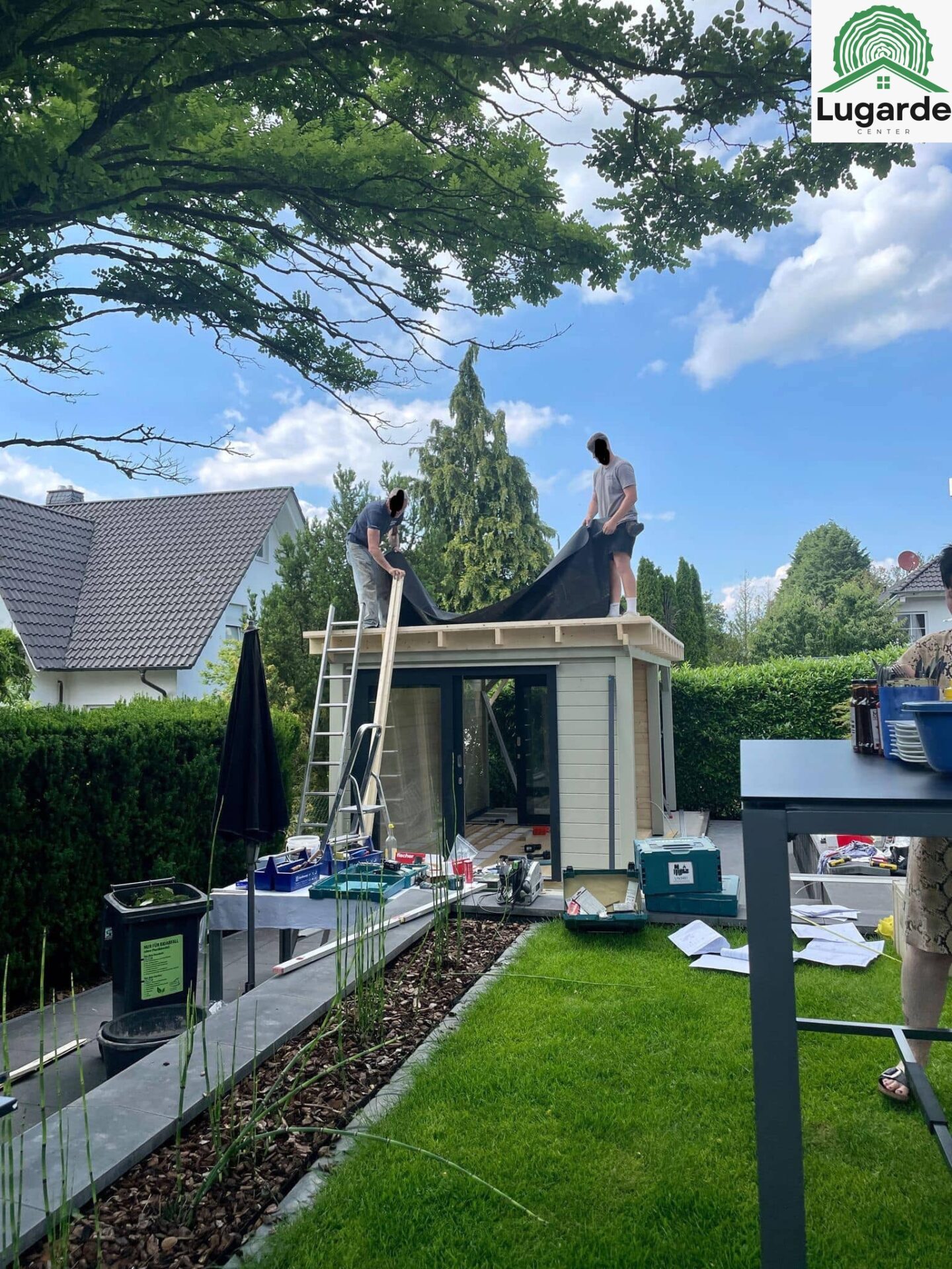 Montage Team am Dachüberstand: Pro System Kieselgrau, Glasfront eingesetzt; Sitzecke und Grillzone klar angelegt.